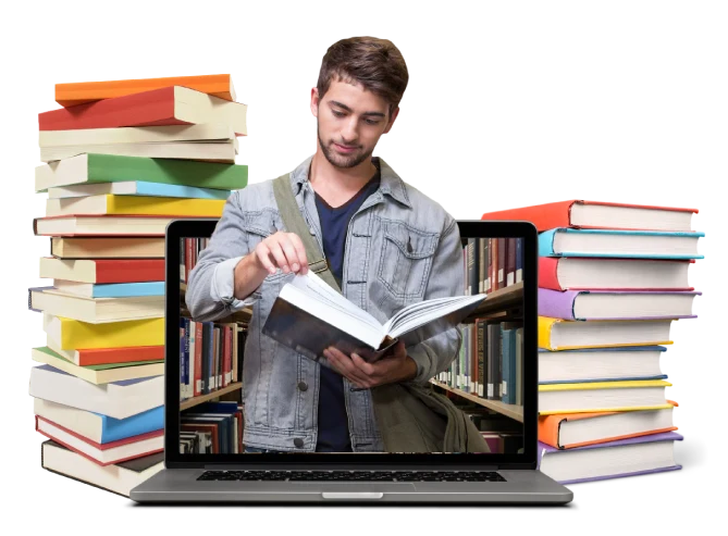 Man reading a book beside a laptop surrounded by stacks of books